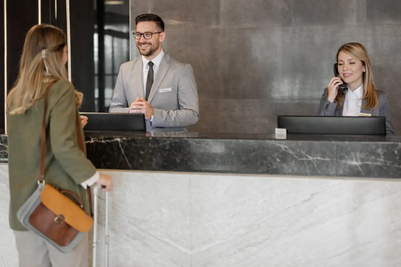 Ospite al check-in davanti al banco della reception mentre la receptionist risponde al telefono
